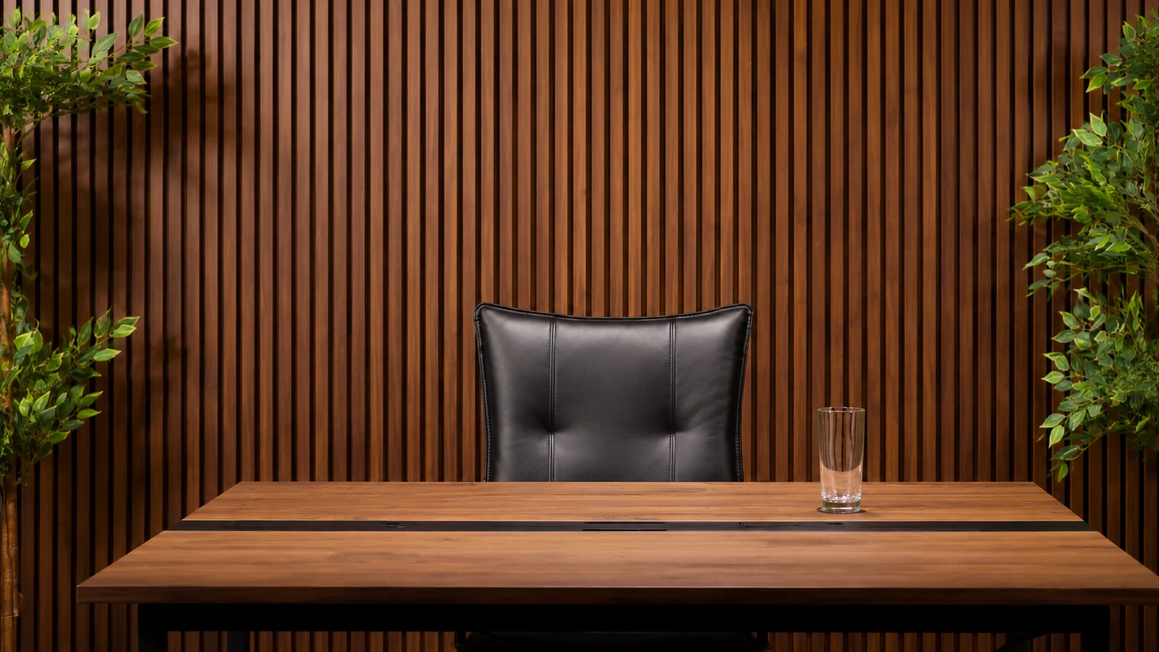 One black office chair behind a walnut desk in The Executive, with walnut slats and plants.