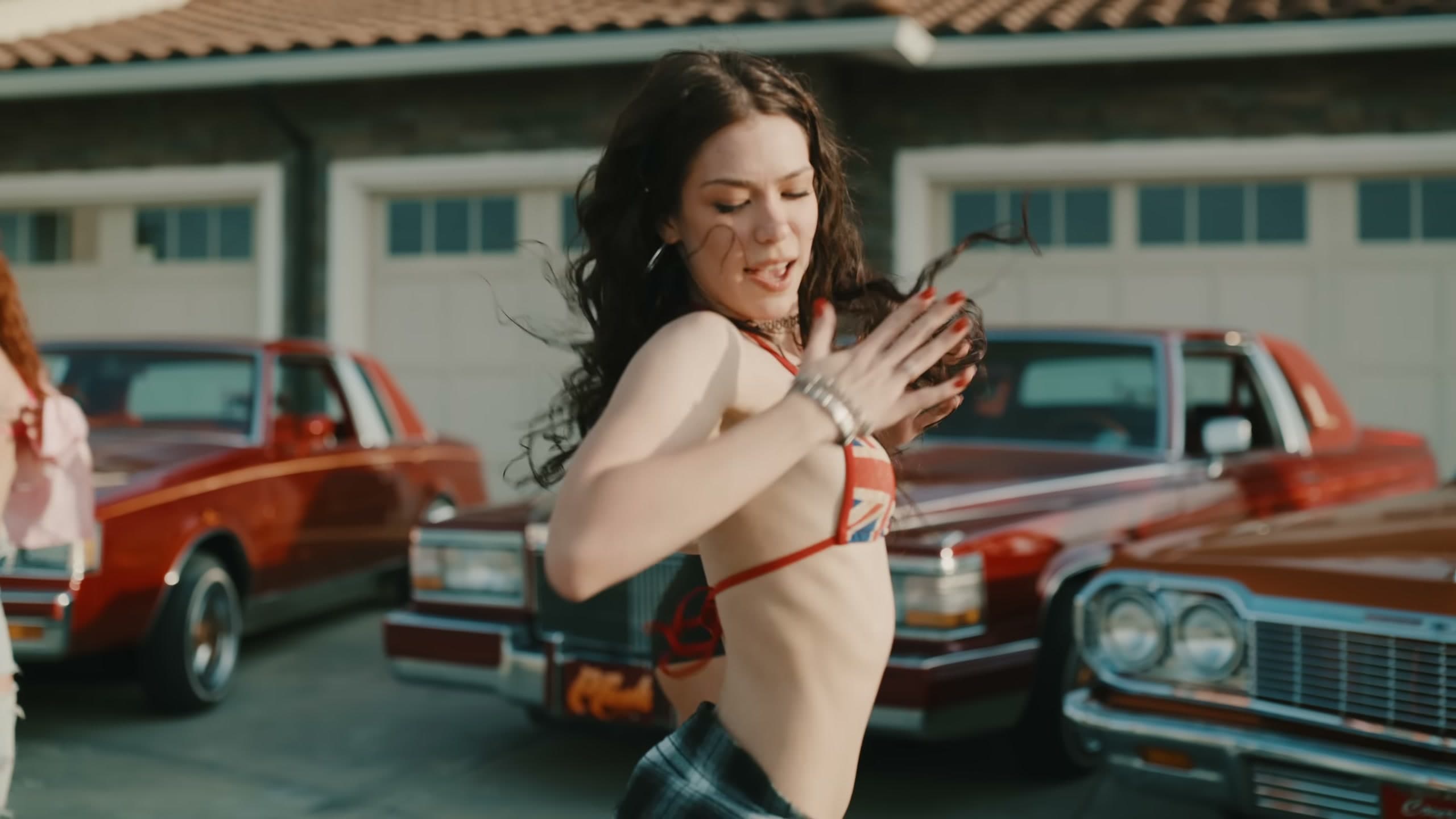 Dancer mid-move in front of red lowriders in the Body Is Tea music video